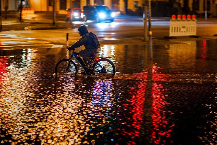 Ein Radfahrer fährt durch das Hochwasser am Stadthafen von Wismar. - © Jens Büttner/dpa