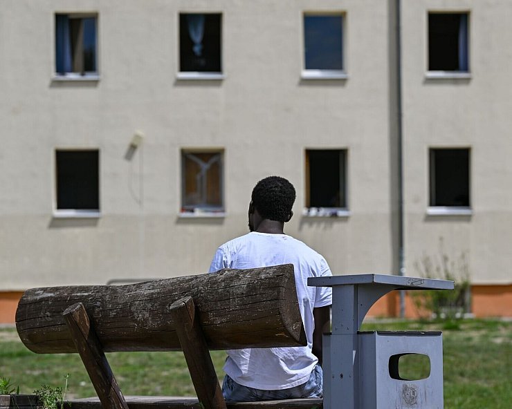 Ein Migrant sitzt auf einer Bank auf dem Gelände der Zentralen Erstaufnahmeeinrichtung für Asylbewerber des Landes Brandenburg in Eisenhüttenstadt. (Archivfoto) - © Patrick Pleul/dpa