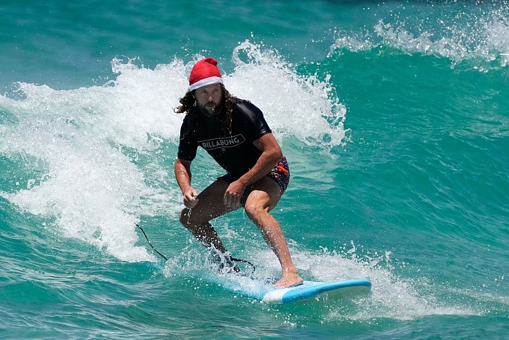 Surfende Santas gehören in Australien zu Weihnachten dazu. (Archivbild) - © Rick Rycroft/AP/dpa
