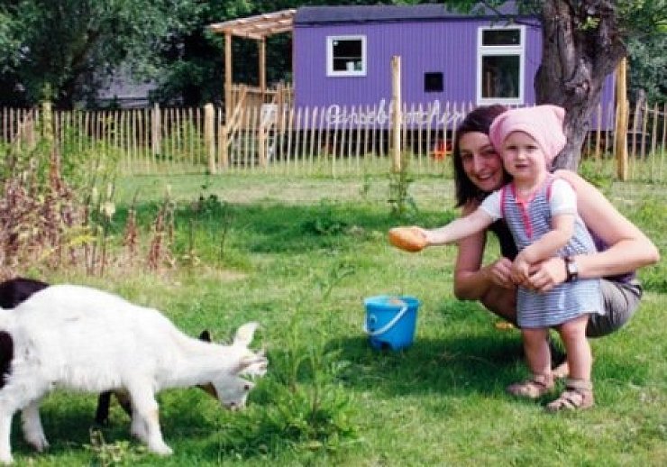Auf Tuchfühlung mit der Hausziege: Jennifer und Lina Bierhenke locken die nur selten bockige "Emmy". Im Hintergrund ist der lila Bauwagen der "Gänseblümchen"-Gruppe auf dem Kastanienhof zu sehen. - © Foto: Stracke
