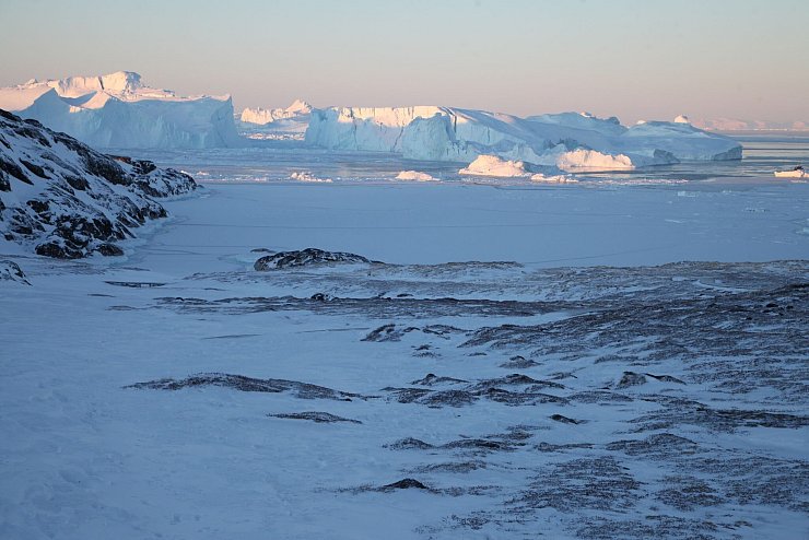 Eisberge ragen im Ilulissat-Eisfjord hinter einer verschneiten Gesteinslandschaft in die Höhe. - © Steffen Trumpf/dpa