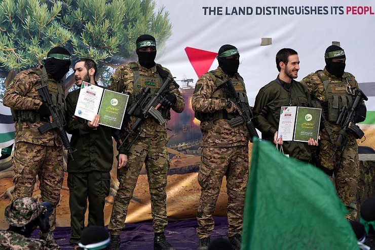 Ein vermummter Hamas-Kämpfer gibt einer israelischen Geisel Anweisungen während einer Übergabe-Veranstaltung im Gazastreifen. - © Abdel Kareem Hana/AP/dpa