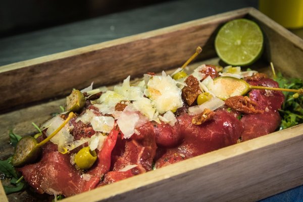 Statt auf dem runden Teller wird das Carpaccio im «The Dry Gin and Beef Club» auf einem kleinen Tablett auf Rucola angerichtet. Limette träufelt der Gast zum Schluss selbst darüber. - © Christin Klose/dpa-tmn