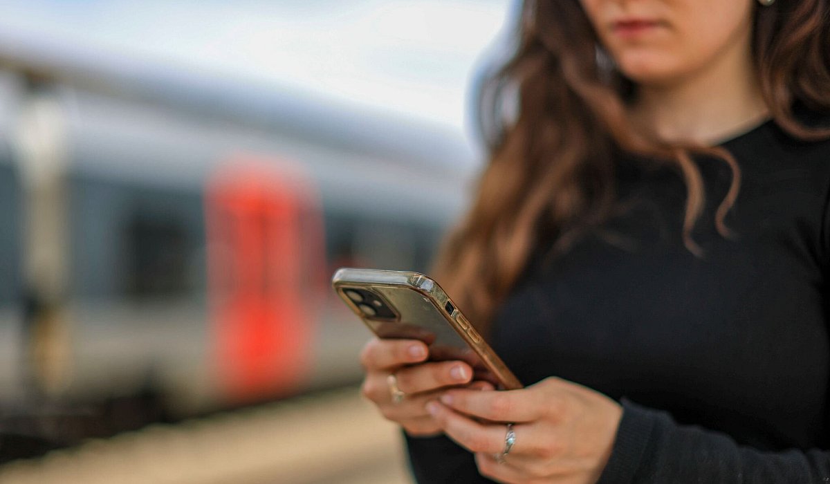 Eine junge Frau steht mit ihrem Mobiltelefon auf einem Bahnsteig - Jan Woitas/dpa/dpa-tmn