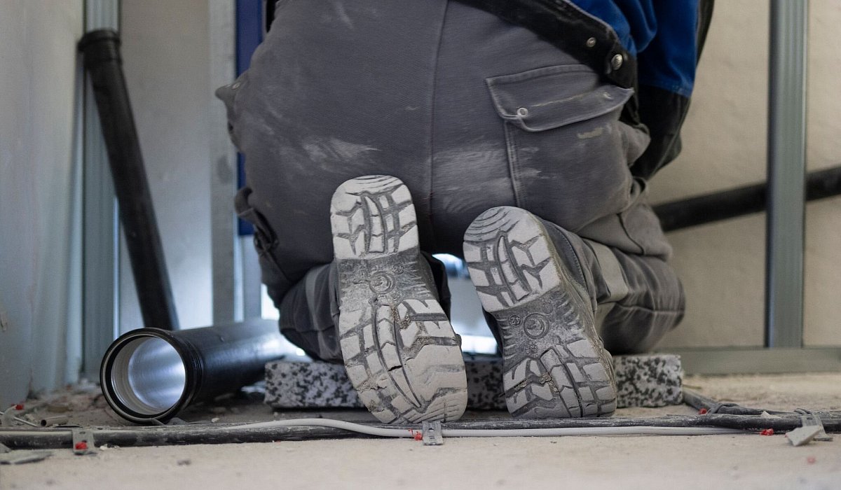 Ein Handwerker arbeitet kniend an der Sanit&auml;rinstallation - Marijan Murat/dpa