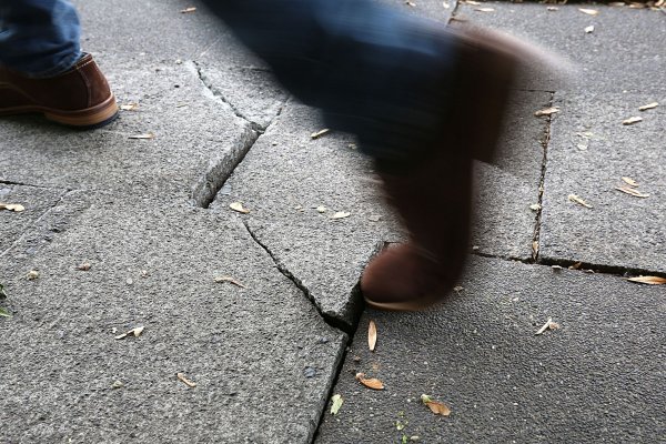 Ein Mann geht auf einem Bürgersteig über eine hochstehende Gehwegplatte. - © Oliver Berg/dpa/Archivbild
