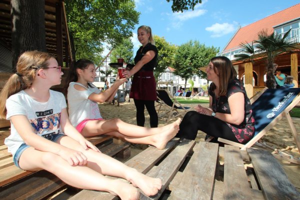 Summer in the City: Servicekraft Runa Keller serviert Katharina Eickhoff mit (von links) Alisa und Marleen Getränke an der „Sandibar" im Lippegarten. Bis in den September läuft nun die Sommergastronomie. - © Till Brand