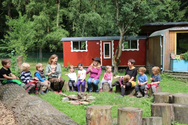 So sieht der Normalfall aus: Waldkindergartenleiterin Jelka Malin Karger (Mitte) und die Erzieherinnen Anke Sjöberg (links) und Lara Trojak singen mit den Kindern im Morgenkreis. Im Hintergrund ist der Bauwagen zu sehen. - © Carolin Brokmann