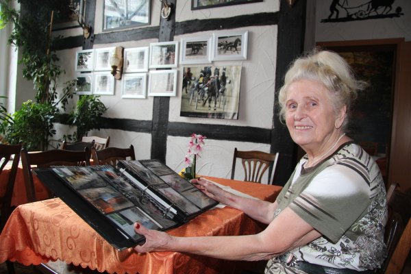 Einst und jetzt: Ingried Steinnagel blättert in dem Fotoalbum, das das Hof-Café im abbruchreifen Rohzustand zeigt. Mit dem schmucken Fachwerkhaus von heute hat es wenig gemein. Die Wand zieren Fotos aus dem Trabrennsport, dem das Trabergestüt Diekhof über Jahrzehnte verbunden war. - © Dieter Asbrock