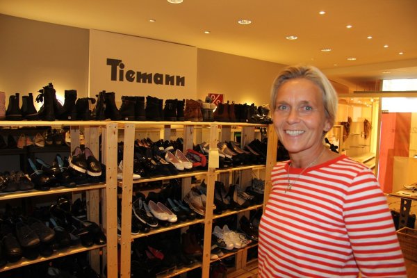 Susanne Tiemann trotzt dem Aus mit einem Lächeln: In den Regalen hinter ihr stehen deutlich mehr Paare als sonst. Das Schuhhaus an der Langen Straße lädt zum Räumungsverkauf. - © Thomas Reineke