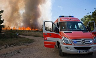 Ein Mannschaftstransportfahrzeug der Freiwilligen Feuerwehr Kostheim steht vor einem brennenden Feld. Wegen der massiven Rauchentwicklung wurde die Autobahn 671 f&uuml;r eine halbe Stunde gesperrt. - Foto: Michael Ehresmann/Wiesbaden112.de