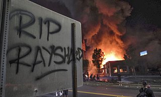 «RIP Rayshard» steht auf einem Schild, während im Hintergrund ein Wendy's-Restaurant brennt. - Foto: Ben Gray/Atlanta Journal-Constitution/AP/dpa