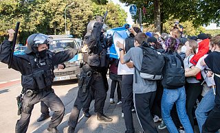 Ein Polizist hebt vor einer Gruppe von Demonstranten seinen Schlagstock. - Foto: Peter Kneffel/dpa Ein Polizist hebt vor einer Gruppe von Demonstranten seinen Schlagstock. - Foto: Peter Kneffel/dpa