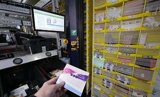 Beim Picken: Der Computer zeigt LZ-Redakteur Jost Wolf auf dem Monitor, dass nun die Plaque-Färbetabletten aus Fach 1E entnommen werden müssen. Zusätzlich wird das Fach quadratisch hell angestrahlt. Das gelbe Regal hat vorher ein Roboter an die Öffnung der Pick-Station gefahren. Die Ware muss nach dem Scannen in eine der schwarzen Kisten gelegt werden. Das wird mit Druck auf den runden schwarzen Knopf darüber bestätigt. - Jost Wolf