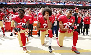 Colin Kaepernick (M.) kniete 2016 mit seinen Teamkollegen Eli Harold (l) und Eric Reid vor einem Spiel der San Francisco 49ers. - Foto: John G Mabanglo/EPA/dpa