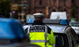 Ein Polizeibeamter steht zwischen zwei Einsatzfahrzeugen der Polizei. - Philipp von Ditfurth/dpa/Symbolbild