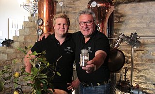 Falk und Friedhelm Begemann vor ihrer Destille. In den Händen halten sie ihre spezielle Gin-Käuter-Mischung. Und auch die Zitronen für das Finish stammen aus eingenem Anbau. - Carolin Brokmann-Förster