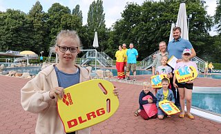 Amelie (10, vorne) hält das Schwimmbrett der DLRG, dahinter ihre Familie mit den Eltern Markus und Anna Peter sowie den Kindern (von links) Simon (5), Lynus (8), Marlene (7) und Luise (9). Dahinter stehen (von links) Bianca Wehmann und Klaus Steinkamp von der DLRG Ortsgruppe Bad Salzuflen sowie Marco Schubert, stellvertretender Bäderbetriebsleiter der Stadtwerke. - Alexandra Schaller