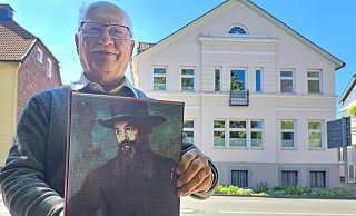 Dr. Hans-Joachim Keil präsentiert die Abbildung eines Porträts von Adolf Neumann-Hofer vor dessen ehemaligen Wohnhaus in der Leopoldstraße. Das Gemälde stammt vom Künstler Bruno Wittenstein (1876-1968), ist um 1920 mit Öl auf Leinwand entstanden und zeigt Adolf Neumann-Hofer mit seinem Markenzeichen: dem langen, dunklen Bart. - Carolin Brokmann-Förster