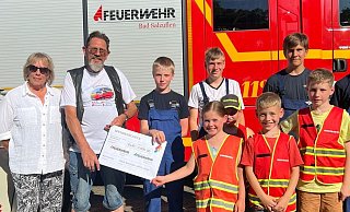 Oldtimer-Fan Klaus Siekmann übergibt einen symbolischen Spendenscheck an die Gruppe 1 der Jugendfeuerwehr Holzhausen. Links steht Siekmanns Lebensgefährtin Petra Werner. - Klaus Siekmann