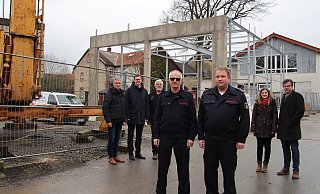 Mit dem Kran (links) entsteht die neue Fahrzeughalle. Darüber freuen sich (von links) Thorsten Paulussen, Matthias Kalkreuter, Andreas Naumann vom Gebäudemanagement, Friedhelm Stölting, Andreas Bicker sowie Janina Fleischhammer und Thorsten Hoffjann vom Architekturbüro Hoffjann. Rechts im Hintergrund ist das bestehende Gerätehaus zu sehen. - Nadine Uphoff