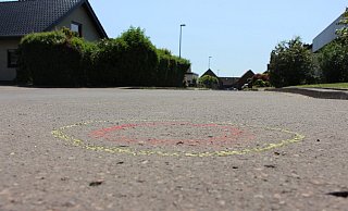 Mehr als 30 gelb-rot markierte Kreise (das Bild zeigt einen davon) auf der Straßendecke in der Salzufler Sackgasse deuten genau auf die Stellen hin, wo die Spurensicherung am Einsatzort Patronenhülsen sichergestellt hat. Fünf Kugeln trafen den immer noch schwer verletzten 19-jährigen Fahrer. - Janet König