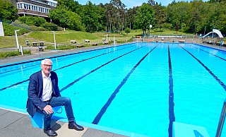 Stadtwerkechef Peter Synowski, der auch für die Bäder zuständig ist, sitzt auf einem der Startblöcke, hinter sich das 50 Meter lange Schwimmerbecken. - Gunter Held