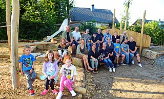 Henry, Malina und Marlene (von links) freuen sich &uuml;ber den neuen Spielplatz, den die Helfer im Hintergrund f&uuml;r sie gebaut und gestaltet haben. - Nicole Ellerbrake