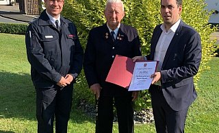 Der Leiter der Feuerwehr Lügde, Michael Schoppmeier (links), und Bürgermeister Torben Blome nehmen August Moseke in ihre Mitte.  - Feuerwehr Lügde