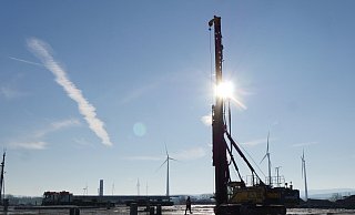 Eine der drei Rammen, die zum Zeitpunkt der Begehung auf der Amazon-Baustelle im Einsatz waren. Davor liegen die Betonpfähle, die von ihr in den Boden getrieben werden. Auf sie kommt dann ein Köcherfundament, in das wiederum die vorproduzierten tragenden Stützen den Gebäudes einbetoniert werden. - Jost Wolf Eine der drei Rammen, die zum Zeitpunkt der Begehung auf der Amazon-Baustelle im Einsatz waren. Davor liegen die Betonpfähle, die von ihr in den Boden getrieben werden. Auf sie kommt dann ein Köcherfundament, in das wiederum die vorproduzierten tragenden Stützen den Gebäudes einbetoniert werden. - Jost Wolf