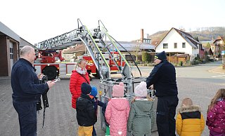 Dirk Köchling (links) und Maik Paskarbeit von der Feuerwehr Lügde haben die große Leiter ausgefahren und den Kindern und Erzieherin Christina Schaper gezeigt, wie die Feuerwehrleute in großer Höhe arbeiten und Menschen in einer speziellen Trage über die Leiter retten können. - Johanniter Lippe-Höxter