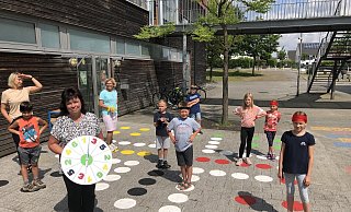 Anke Brand (im Vordergrund mit einer "Würfel"-Scheibe) hat mit OGS-Kindern aus Knetterheide in den Sommerferien ein lebendiges "Mensch-Ärgere-Dich-nicht-Spiel" auf dem Pausenhof aufgebracht. - Thomas Reineke