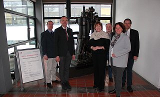 Prof. Dr.-Ing. Georg Heinrich Klepp, Prof. Dr. Jürgen Krahl, Hildegard Müller, Prof. Dr.-Ing. Thomas Schulte, KerstinVieregge, MdB, und Prof. Dr. Stefan Witte (von links) versammeln sich fürs Foto vor Deutschlands ältestem betriebsfähigen Dieselmotor, der in der TH OWL ausgestellt ist. - TH OWL