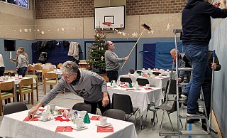Gisela Stöcker richtet auf den Tischen die letzten Details, Rainer Deppe schwingt den Besen, um die Sterne auszurichten. Jan Lüdecke und Erno Stöcker(rechts) haben sie auf die Leine gefädelt. Am Samstag waren 90 ältere Hagener eingeladen, zwei schöne Stunden in der Schulturnhalle zu verleben. - Astrid Sewing