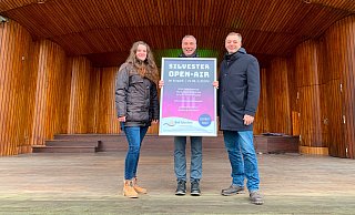 Leonie Immel (von links, Eventmanagement), Bürgermeister Dirk Tolkemitt und Oliver Siekmann (Stadtmarketing) präsentieren das Plakat zum Silvester Open-Air in der Konzertmuschel im Kurpark. - Stadt Bad Salzuflen