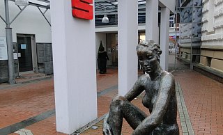 Seit 1929 bewacht „Die große Sitzende", eine etwaein Meter große Bronzeskulptur des Künstlers Georg Kolbe (1877-1947), den Eingang zur Sparkasse. - Hajo Gärtner