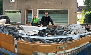 Nathalie Witt und Max König stehen vor einer von vier großen Mulden mit Abfall aus dem vollgelaufenen Keller ihres Hauses (im Hintergrund). - Thomas Reineke