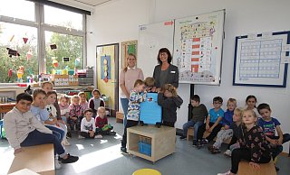 Die Kinder aus der Drachenklasse von Lehrerin Jessica Brinkmann (links) bekommen von Beate Becker den Bücherkoffer überreicht. Danilo, Keno und Luisa versuchen, einen Blick auf den Inhalt zu erhaschen. - Linda Schnepel