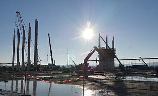 Auf die in den in den Boden getriebenen Betonpfähle kommt ein Köcherfundament, in das wiederum die vorproduzierten tragenden Stützen den Gebäudes einbetoniert werden. Die Wand rechts (mit der Kletterverschalung) ist aus Stablitätsgründen nicht aus Fertigbetonteilen zusammengesetzt, sondern komplett vor Ort betoniert worden. - Jost Wolf