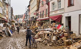 In Ahrweiler in Rheinland-Pfalz schiebt eine Frau ihr Fahrrad durch den Schlamm. Anwohner und Ladeninhaber versuchen, ihre Häuser vom Dreck zu befreien und unbrauchbares Mobiliar nach draußen zu bringen. - Thomas Frey/dpa In Ahrweiler in Rheinland-Pfalz schiebt eine Frau ihr Fahrrad durch den Schlamm. Anwohner und Ladeninhaber versuchen, ihre Häuser vom Dreck zu befreien und unbrauchbares Mobiliar nach draußen zu bringen. - Thomas Frey/dpa