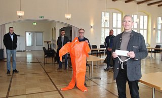 Bürgermeister Stefan Rother (vorne) zeigt einen einfachen Mundschutz der Firma Vorndamme (Isotemp), Heinz Blome (Ordnungsamt) einen orangen Schutzoverall. Im Hintergrund (von links) Rainer Holste (Ordnungsamt), Tim Sölter (Zentrale Dienste) und Stephan Beinker (Baubetriebshof/Feuerwehr). - Dieter Asbrock