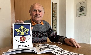 Heimatverbunden: Albert Siegert in seiner Küche mit den von ihm zusammengetragenen Aufzeichnungen und dem Wüstener Wappen.  - Sven Kienscherf