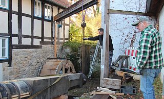 Lars Kine (links) und Dieter Knaup bugsieren die Antriebswelle vom Anh&auml;nger vor das neue M&uuml;hlrad. - Nadine Uphoff