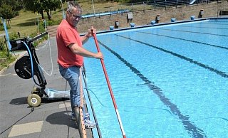 Schwimmmeister Dirk Seifert reinigt den Beckenrand mit dem langen Besen. - Karin Prignitz