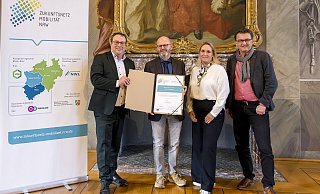 Urkundenübergabe an die neue Mitgliedskommune Blomberg im Zukunftsnetz Mobilität NRW: (von links) Verkehrsminister Oliver Krischer, Detlef Wehrmann (Stadt Blomberg), Daniela Niestroy-Althaus (Leiterin der Koordinierungsstelle Westfalen-Lippe des Zukunftsnetz Mobilität NRW) und Joachim Künzel (Geschäftsführer des Nahverkehr Westfalen-Lippe). - „go.Rheinland GmbH/Smilla Dankert“