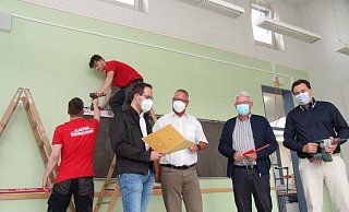 Joel Ollermann (von links) und Luca Klausing von der Firma Elektro Dresselhaus schrauben Kabelkanäle an die Wände eines Klassenzimmers, während Bauamtsleiter Manuel Bröker, Maik Czarnecki aus dem Fachbereich Bildung, Soziales und Sport, Bürgermeister Thomas Katzer und Kämmerer Patrick Herrmann einen Blick in die Pläne werfen. - Nadine Uphoff