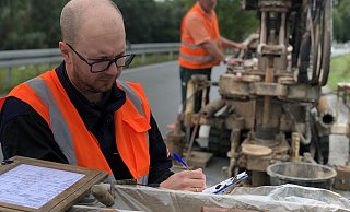 Projektgeologe Niko Miera macht eine erste Sichtungsprobe des Gesteins, auf dem die neue B 66 zwischen Barntrup und Großenmarpe einst verlaufen soll. Im Hintergrund holt der Kollege mit dem Bohrgerät Meter um Meter aus dem Untergrund hervor. - Till Brand