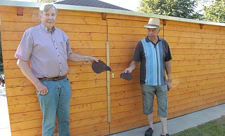 Hartmut Laumeier (links) und Jürgen Reese haben noch zwei der ausgerissenen Dachschindeln auf der Siekwiese gefunden. Die Tür der Hütte hinter ihnen ist notdürftig verschraubt, um weitere Diebstähle zu verhindern. - Carolin Brokmann-Förster