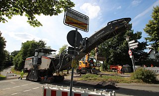 Die Asphaltfr&auml;se frisst sich an der Einm&uuml;ndung der Stra&szlig;e "Im neuen Land" durch den Fahrbahnbelag. Im Hintergrund wartet eine Armada Sattelschlepper, um die Asphaltreste abzutransportieren. - Jens Rademacher