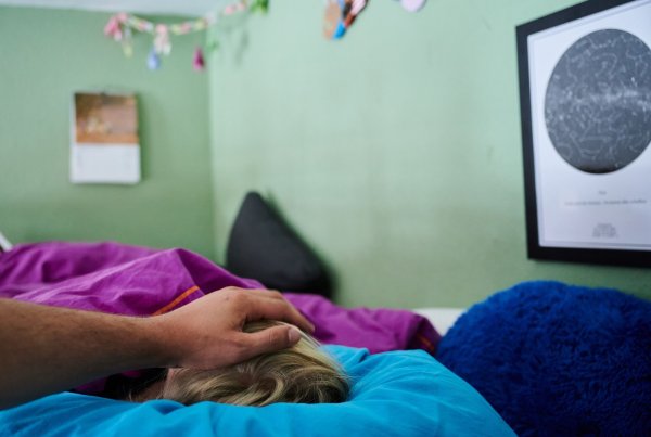 Ein Vater legt seine Hand auf den Kopf eines Kindes, das im Bett liegt. - © Annette Riedl/dpa/Symbolbild
